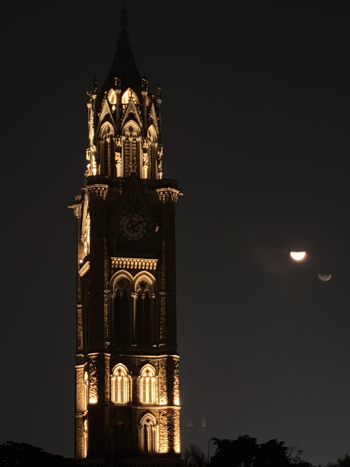 A clock tower lit at night under the moon